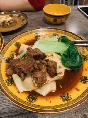 Beef hand pulled noodles served with pak choi on a yellow plate with Chinese characters