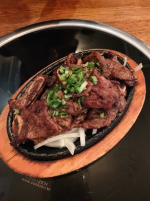 Galbi beef ribs garnished with spring onions served on a bed of onions on a black plate
