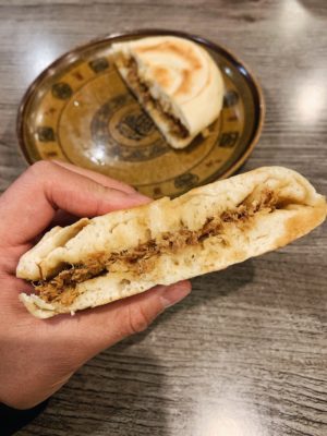 Hand holding half a pork burger with another half served on a plate in the background
