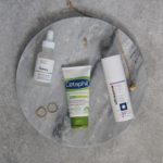 Aerial view of skin care products laid out on a marble slab surrounded by jewellery