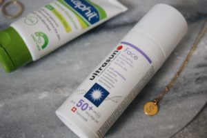 Close up of Ultrasun SPF50, gold necklace with S initial and Cetaphil SPF 50 moisturiser